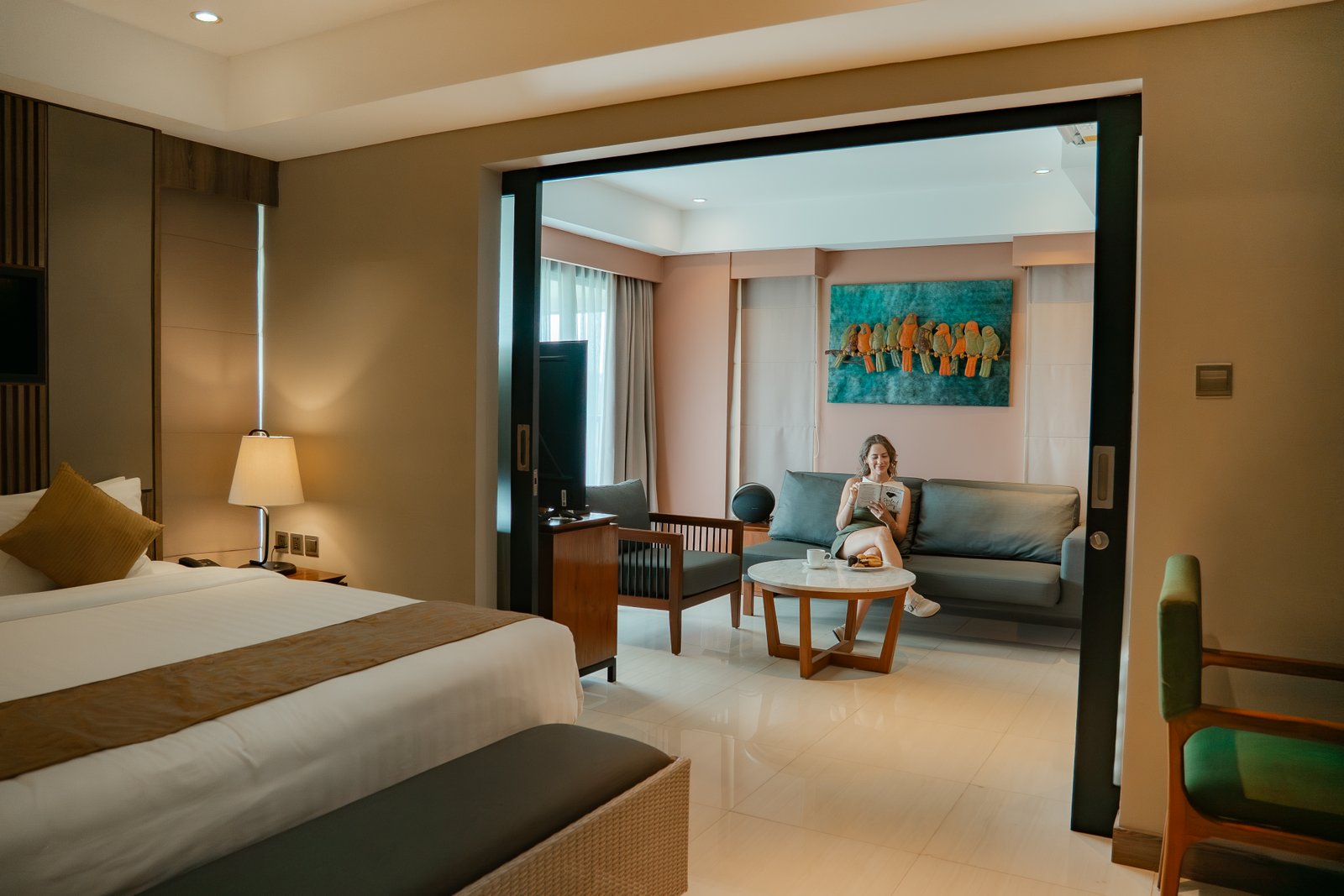 Exterior wide-angle shot of the hotel facade showing a guest relaxing on a private balcony from a distance.