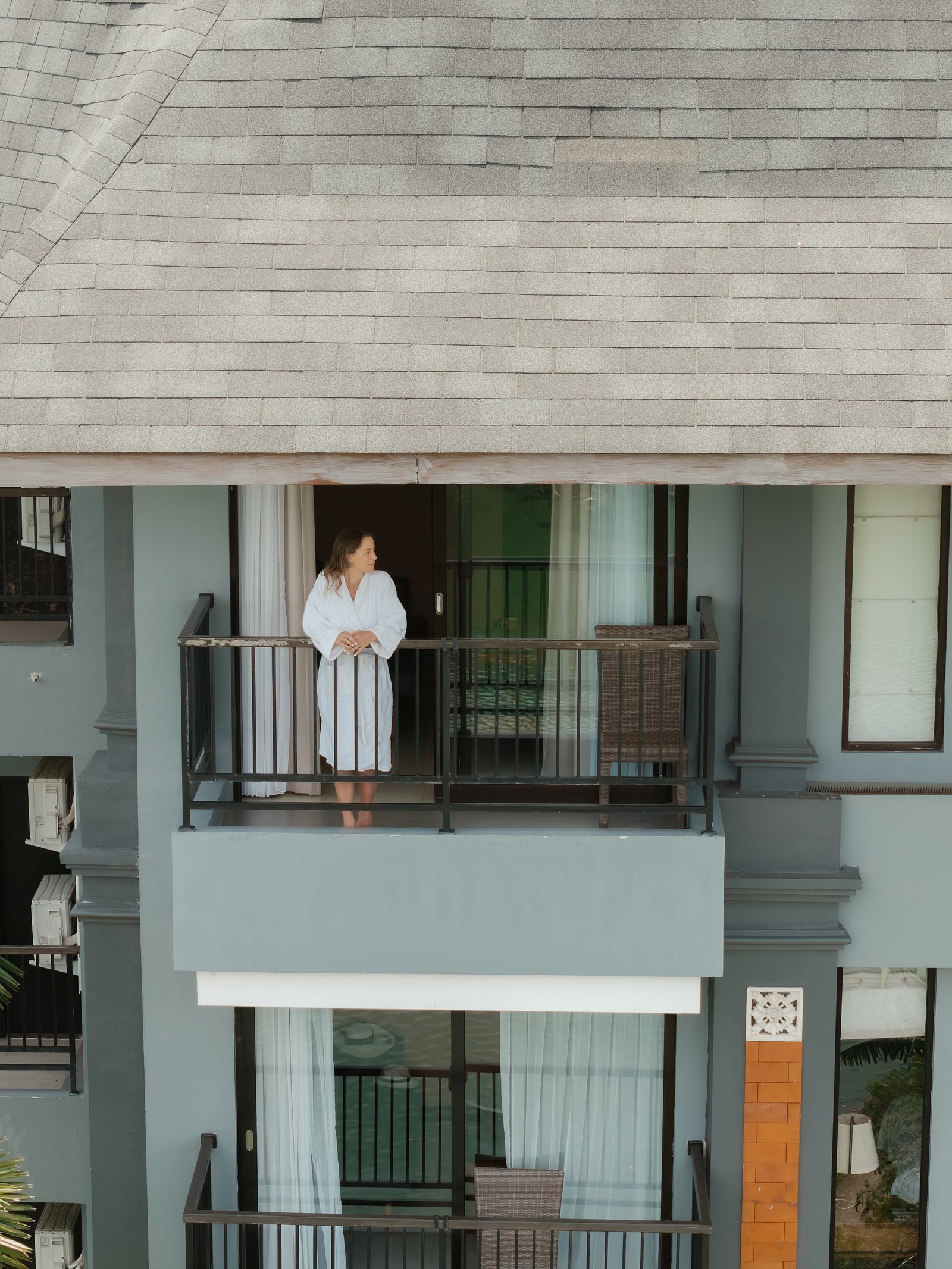 Exterior wide-angle shot of the hotel facade showing a guest relaxing on a private balcony from a distance.