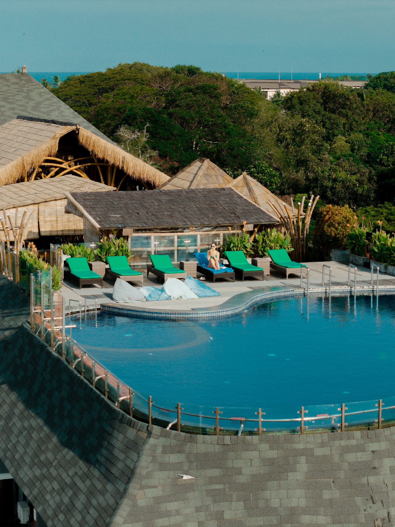 Exterior wide-angle shot of the hotel facade showing a guest relaxing on a private balcony from a distance.